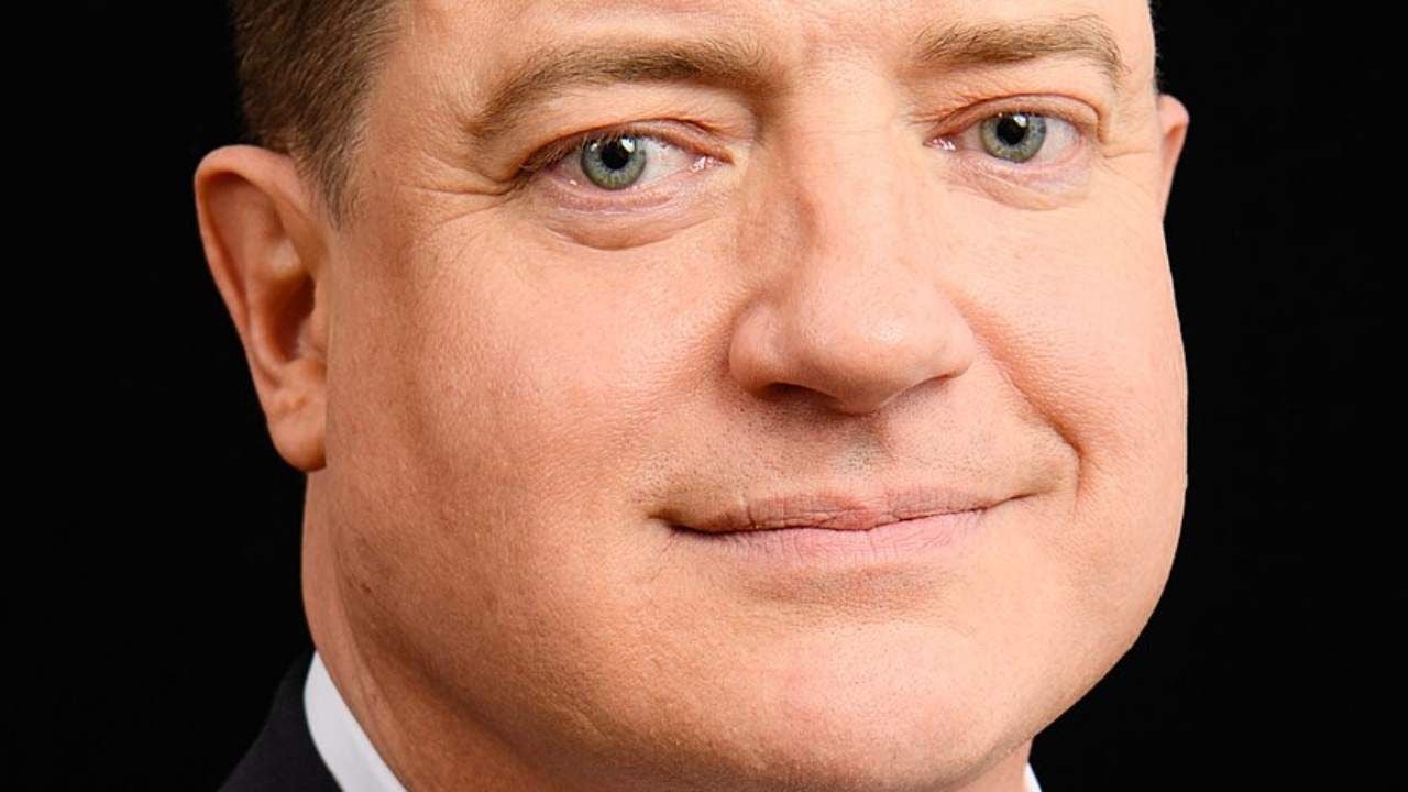Brendan Fraser sonriendo con un traje oscuro, mirando a la cámara en un evento público.